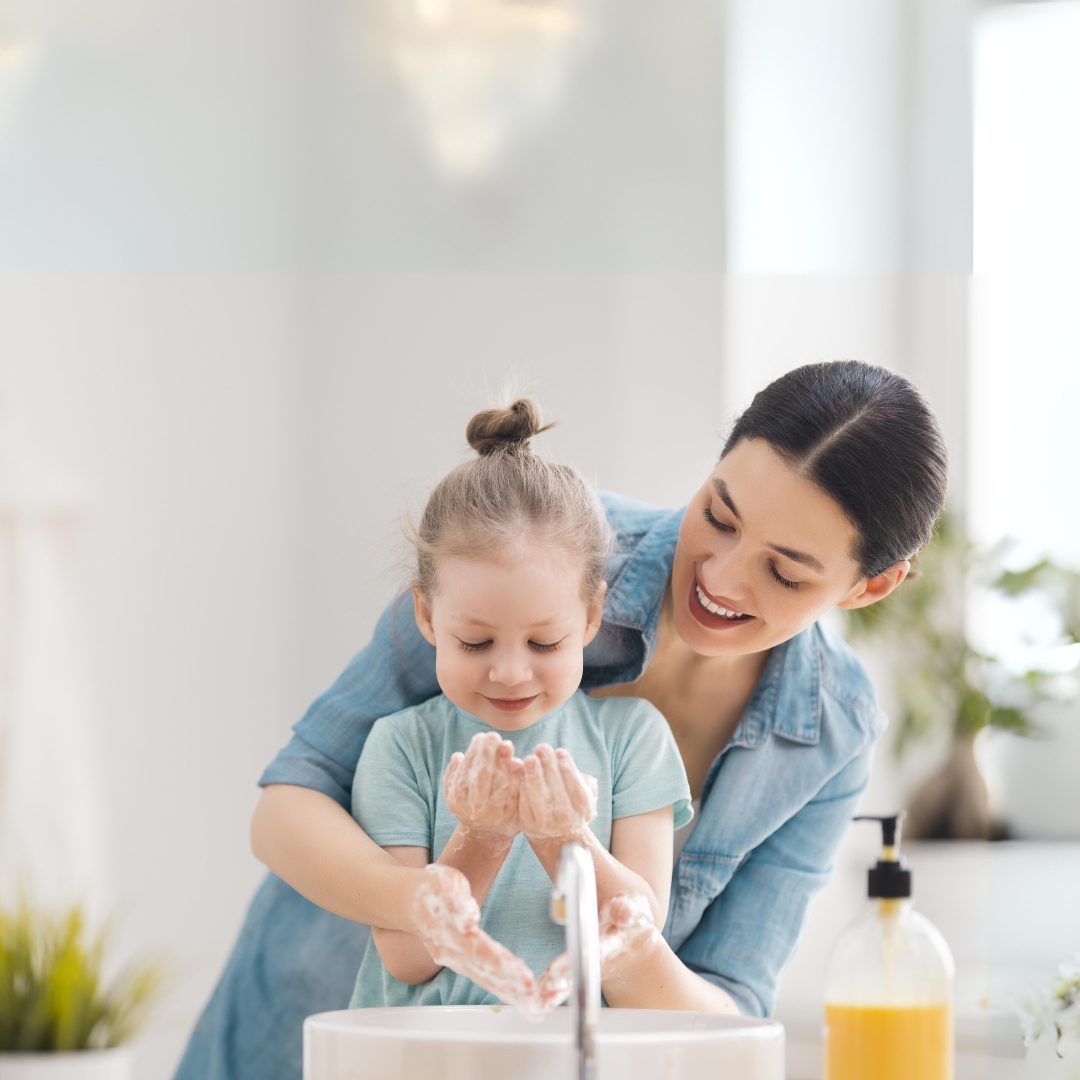 A mother helps her daughter wash her hands.